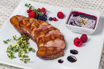 Grilled meat with sauce and berries on a square white plate