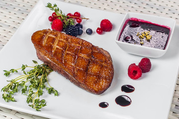 a piece of roasted meat with sweet sauce and berries on a white plate