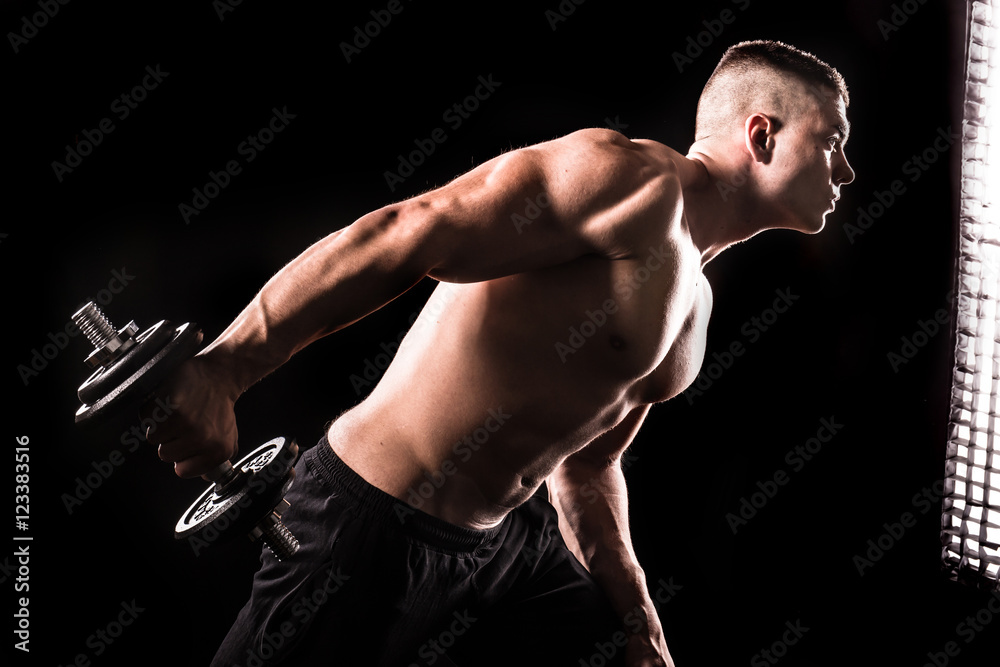 Wall mural muscular young man lifting weights on isolated with black background