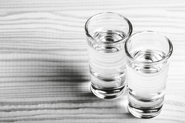 Two vodka shot filled with alcohol on wooden white bar.