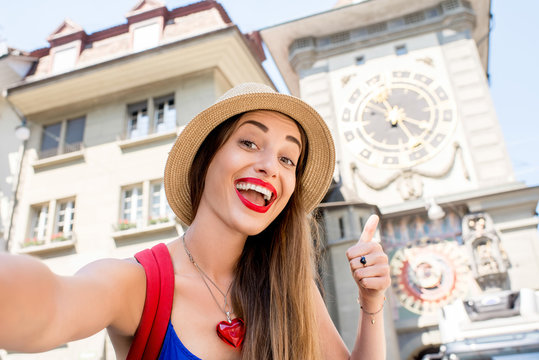 Young female tourist making selfie photo in front of the famous clock tower in the center of the old town of Bern city in Switzerland. Having a great vacations in Switzerland