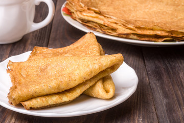 thin pancakes on a white plate with wood background