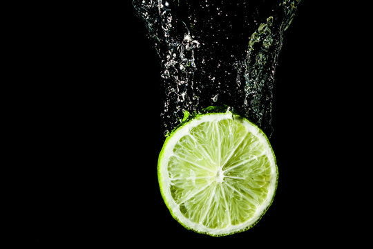 Green lime slice splashing into water.
