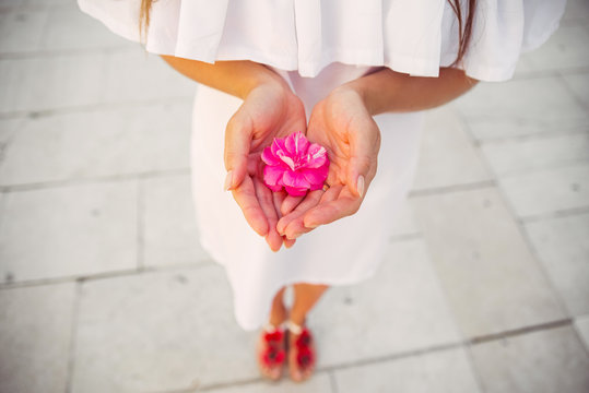 A woman in a white dress holding a flower in the hands
