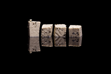 Four cubes of tofu with basil isolated on black reflective background