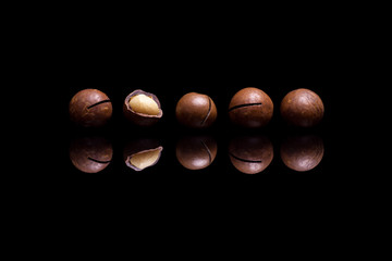 Five macadamia nuts isolated on black reflective background