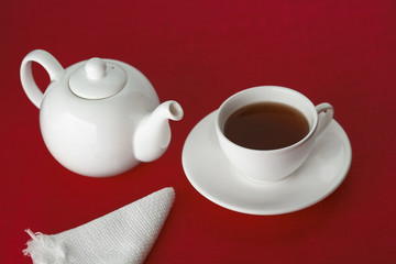 On the deep red background teapot, Cup with saucer and napkin. White 

dishware on Burgundy background. Tea in a white Cup. Studio photos