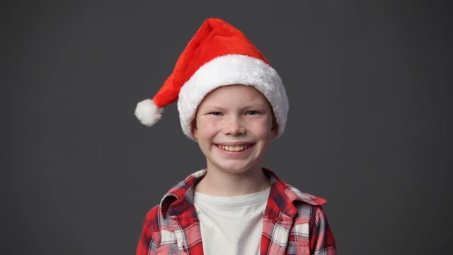 Close up smiling little boy in a red santa's cap against gray background