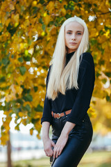 Young stylish sporty blond beautiful teen girl in black posing at park on a warm fall day against blurred yellow foliage background