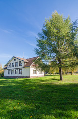 Fototapeta na wymiar Autumn landscape with white holiday cottage, lawn and pine with blue sky background. Near the house there are bicycles and a shop.
