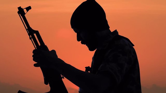 Silhouette of man with gun preparing for battle at dawn