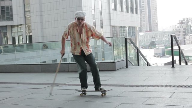 Old man with a cane riding on a skateboard.