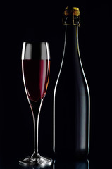 Bottle of red wine with a glass on a black background in low key
