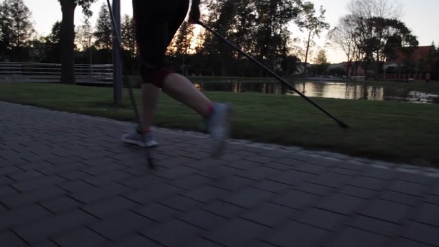 Nogi dziewczyny uprawiającej nordic walking w parku o zmierzchu.