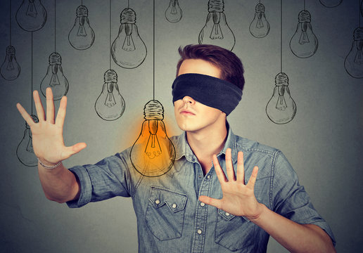 Blindfolded man walking through light bulbs searching for idea
