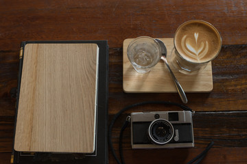 hot fresh coffee in see through glass water glass retro camera and wooden notebook on wooden tray and table at coffee time / hot fresh coffee and camera