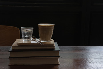 hot fresh coffee in see through glass water glass on big book on wooden tray and table silver spoon at coffee time / hot fresh coffee and book