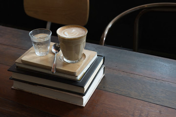 hot fresh coffee in see through glass water glass on big book on wooden tray and table silver spoon at coffee time / hot fresh coffee and book