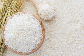 White rice in bowl and a bag, a wooden spoon and rice plant on white rice background, Top view with...