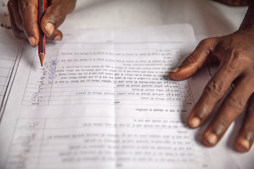 Hands of a farmer in India who fills out an application in Hindi language asking for infrastructure...