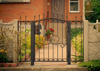 Red house facade with iron fence, green trees and flowers