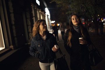 Fototapeta na wymiar Two fashionable girlfriends walking in city avenue at night
