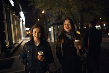 Two fashionable girlfriends walking in city avenue at night