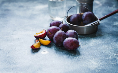 Composition of fresh plums  with kitchenware over a grey table