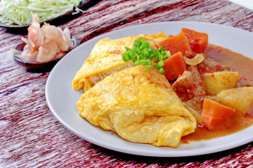 Close up of omelet rice topped Japanese yellow curry  with sliced cabbage and pickled ginger. Selective focus.