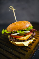 Tasty grilled beef burger in crispy shortbread with lettuce and fresh vegetables on stone dark background. Street food with space for text.