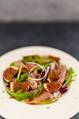 Figs and prosciutto with arugula leaves served on a plate. 