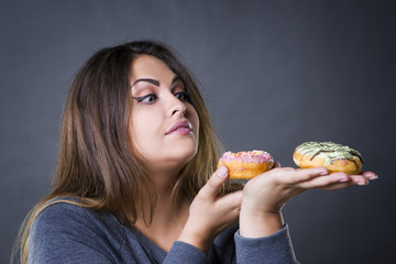 Beautiful young caucasian plus size model posing with donuts on a gray studio background