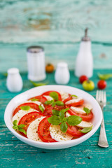 Delicious caprese salad with ripe tomatoes and mozzarella cheese with fresh basil leaves. Italian food.
