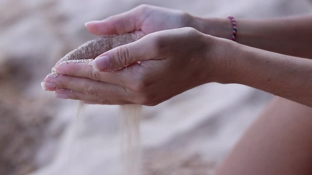 Close up view of a girl's hands with white sand filtering through her fingers while sitting on a beach. Bali, Indonesia. Near the ocean. Beautiful background. Time.