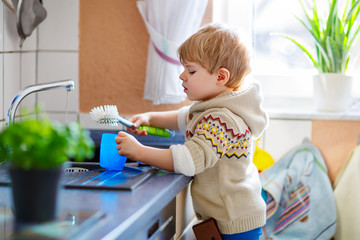 Little toddler helping in kitchen with washing dishes