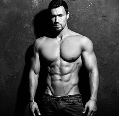 Portrait of strong healthy handsome Athletic Man Fitness Model posing near dark gray wall