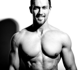 Portrait of strong healthy handsome Athletic Man Fitness Model posing near white wall
