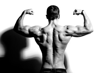 Portrait of strong healthy handsome Athletic Man Fitness Model posing near white wall, flexing his...