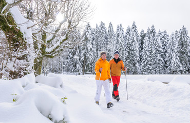 zwei walkende Senioren in tief verschneiter Winterlandschaft