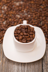 small white cup with coffee beans on wooden background