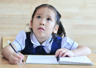 little schoolgirl littening lesson  hold pencil on notebook the table school uniform