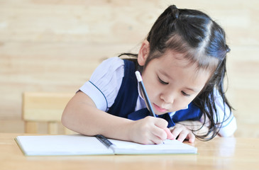 Naklejka premium little girl writeng the notebook with pencil on the table school uniform