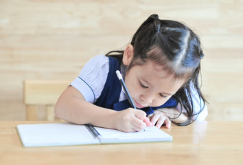 Naklejka premium little girl writeng the notebook with pencil on the table school uniform