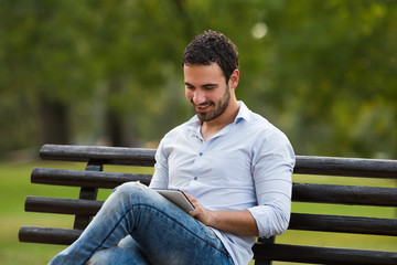 Fototapeta premium Young businessman is sitting at the park and using digital tablet. 