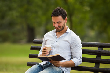 Young businessman enjoys is on a coffee break and he enjoys reading a book and sitting at the...