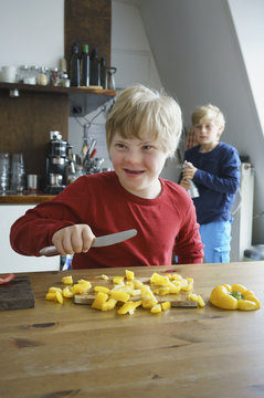 Happy disabled boy chopping yellow bell peppers with brother in background at kitchen