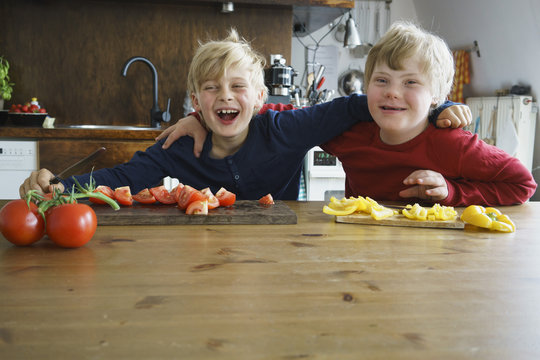 Portrait of happy brothers sitting at table with vegetables in kitchen