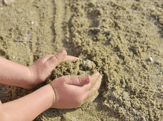 Kid playing with sand on a beach at sunset, starting to build a castle