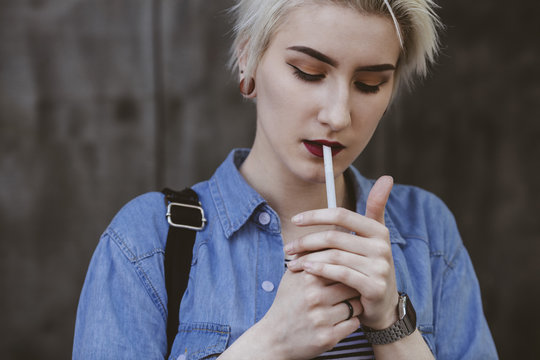 Young fashionable woman smoking cigarette while standing outdoors