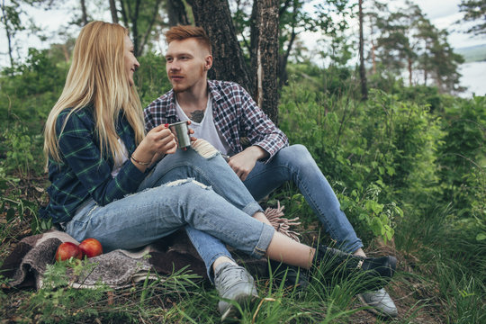 Man looking at girlfriend holding mug while resting below tree at forest